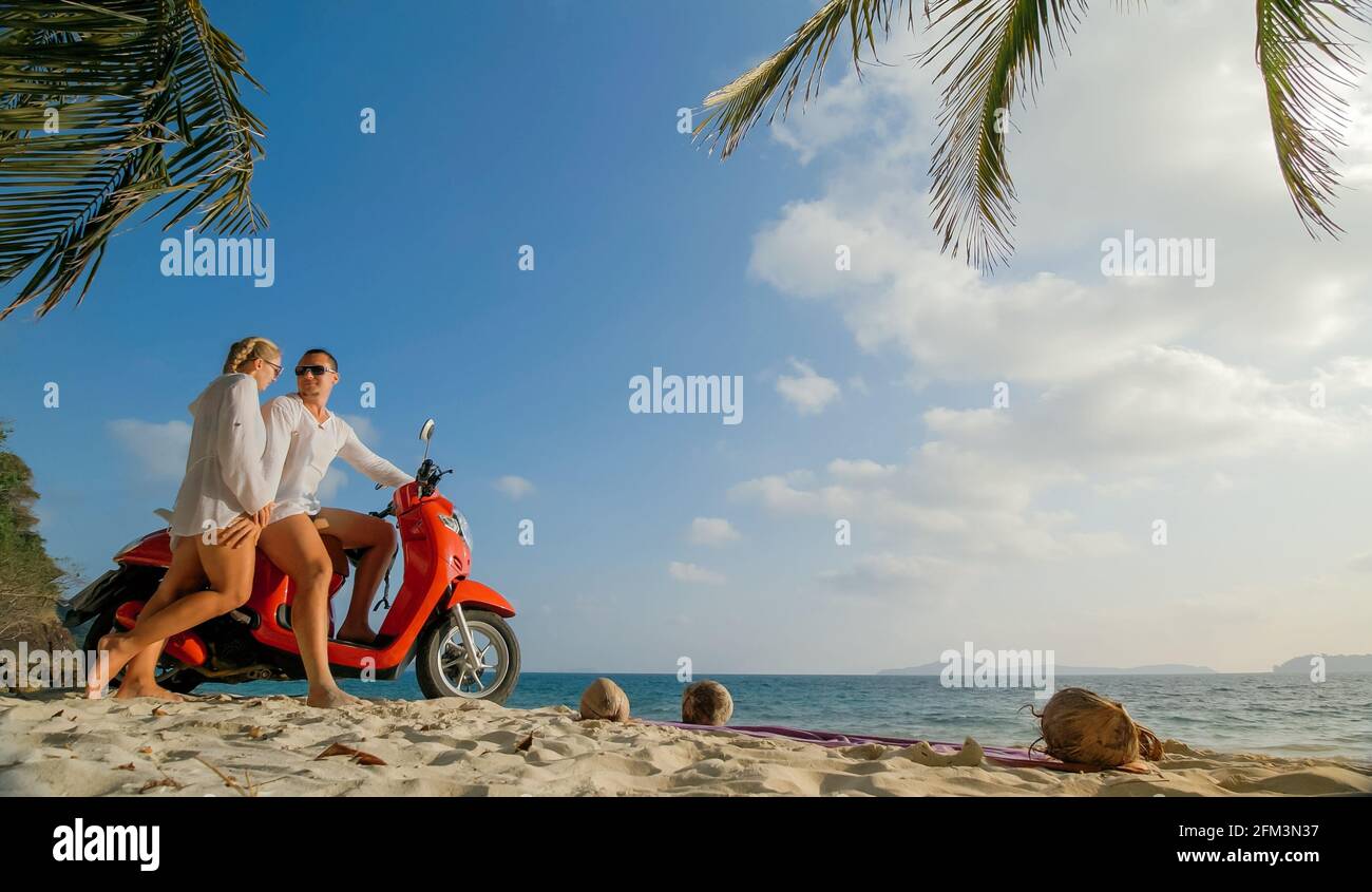 Motorroller Road Trip. Schönes Paar auf rotem Motorrad in weißen Kleidern am Sandstrand. Menschen, die in der Nähe der tropischen Palmen, Meer. Motorradmiete. Stockfoto