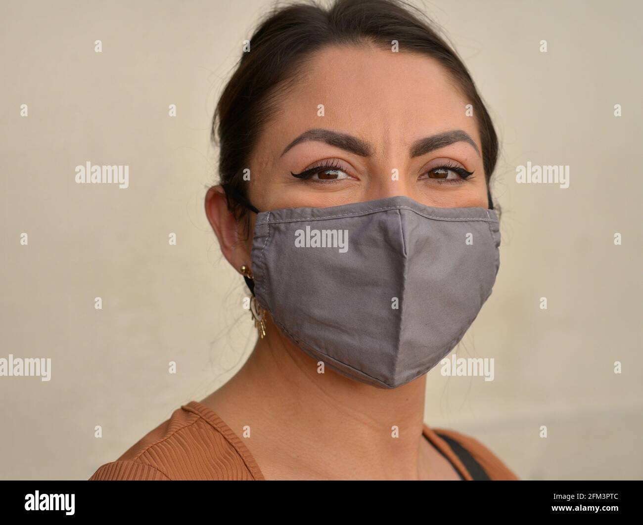 Die junge mexikanische Frau mit schönen braunen Augen und stilvollem Augen-Make-up trägt während der Corona-Virus-Pandemie eine graue Gesichtsmaske aus nicht medizinischem Stoff. Stockfoto