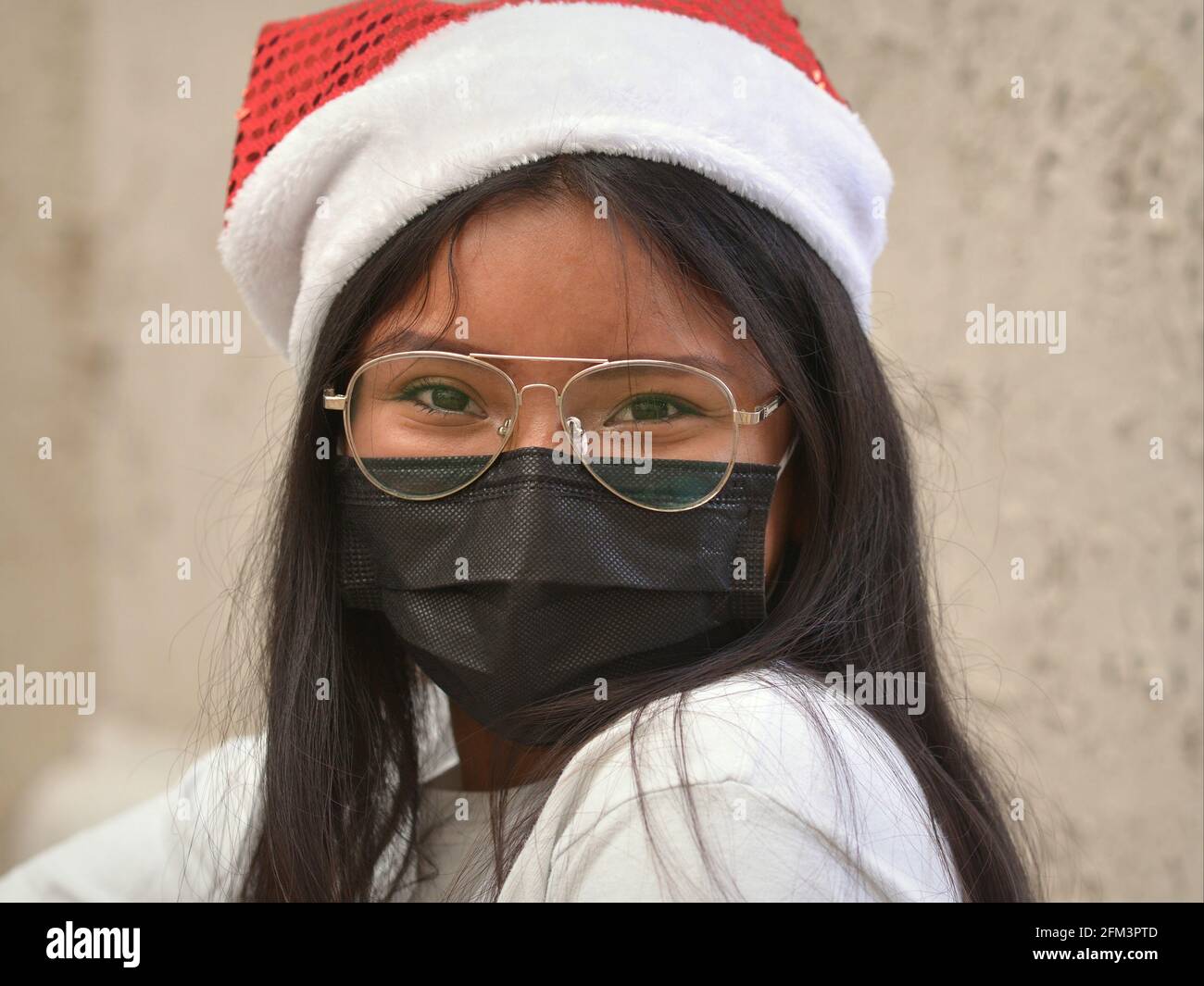 Das langhaarige Teenager-Mädchen mit Fliegerbrille trägt einen lustigen Weihnachtsmann-Hut und eine schwarze Einweg-Gesichtsmaske während der Corona-Virus-Pandemie. Stockfoto