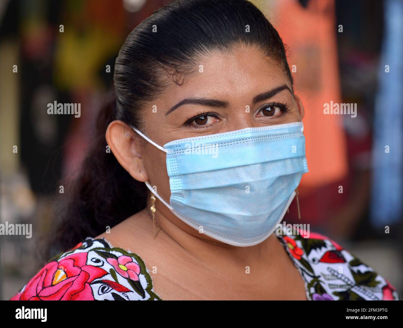 Eine mexikanische Frau mittleren Alters mit schönen braunen Augen trägt während der globalen Corona-Virus-Pandemie eine hellblaue Einweg-OP-Ohrbügel-Gesichtsmaske. Stockfoto