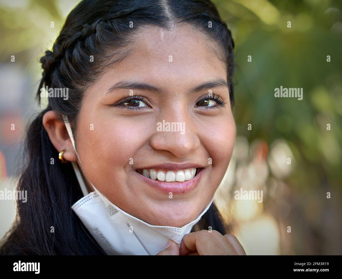 Lächelnd glücklich optimistisch Mexikanisch junge Brünette Latina Frau mit schönen braunen Augen zieht ihre KN95 Gesichtsmaske nach unten und schaut auf den Betrachter. Stockfoto