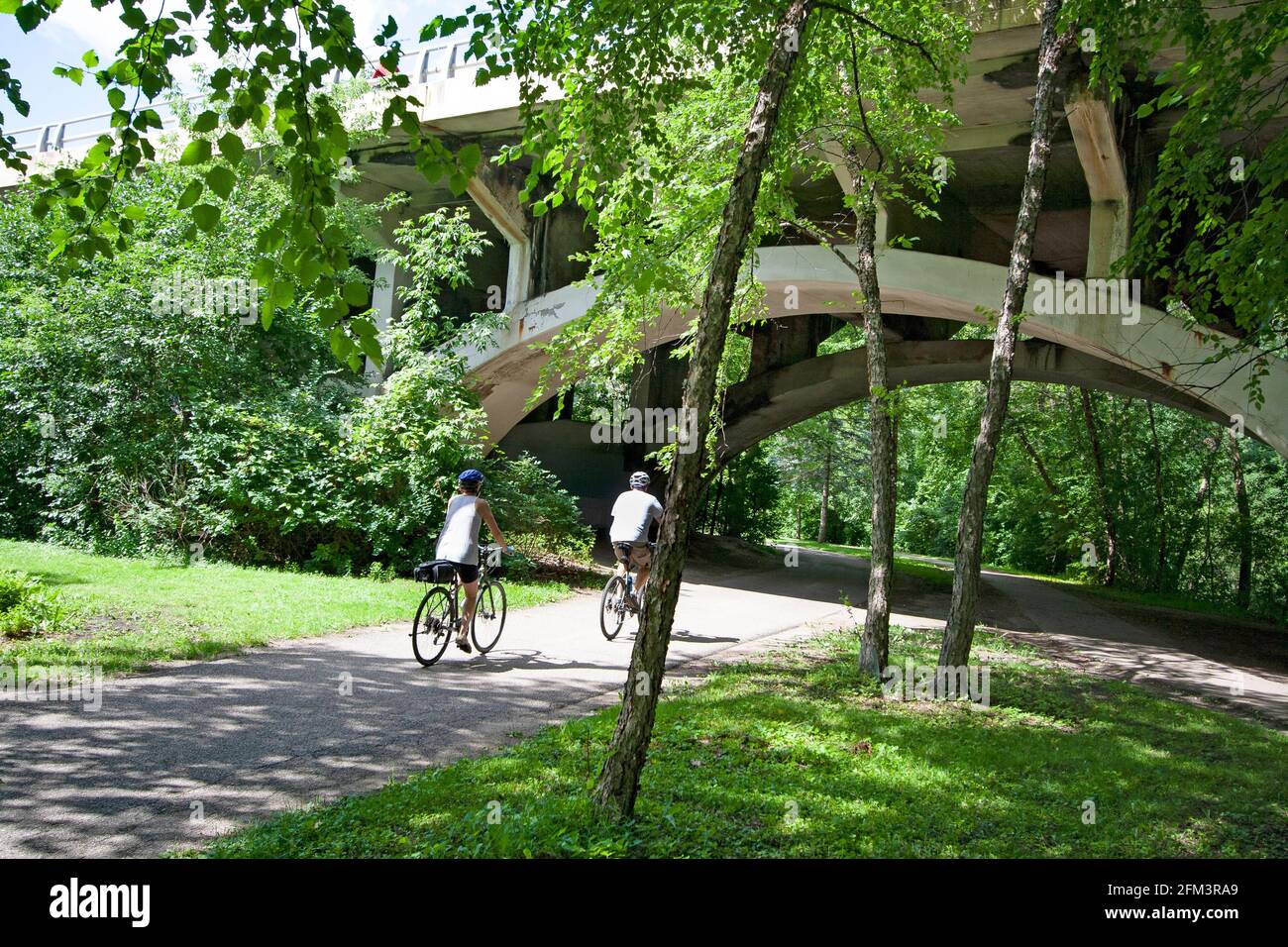 Fahrradfahrer, die entlang des Minnehaha Parkway Regional Trail fahren und unter einem der Bögen der Nicollet Avenue Bridge vorbeifahren. Minneapolis Minnesota, USA Stockfoto