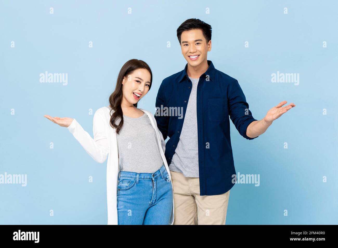 Ankündigungs-Porträt von glücklich fröhlich genial asiatische Paar mit groß Lächelt und öffnet die Hände auf einem isolierten hellblauen Hintergrund Stockfoto