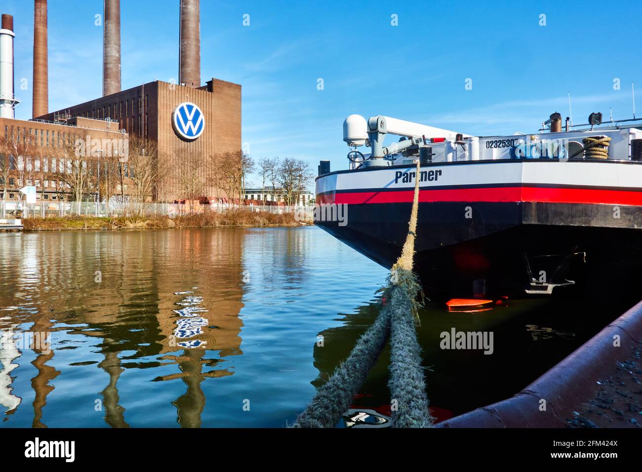 Das Frachtschiff ist mit einem dicken Seil an den Pier gebunden, während sich das Kraft-Wärme-Kopplungs-Kraftwerk von VW im Wasser des Kanals in Wolfsburg widerspiegelt Stockfoto