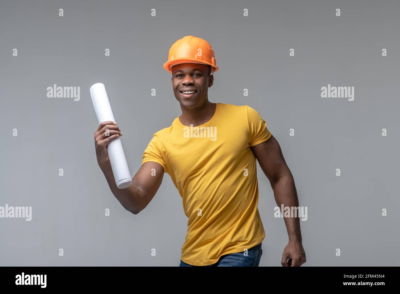 Fröhlicher Mann im Bauhelm mit Papierrolle Stockfoto