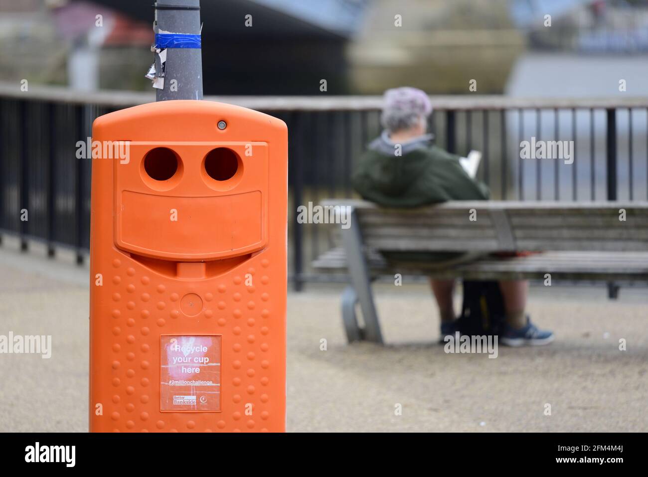 London, England, Großbritannien. Lächelnder Recyclingbehälter und ein Mann, der auf der South Bank liest - Teil der #2-Millionen-Herausforderung Stockfoto