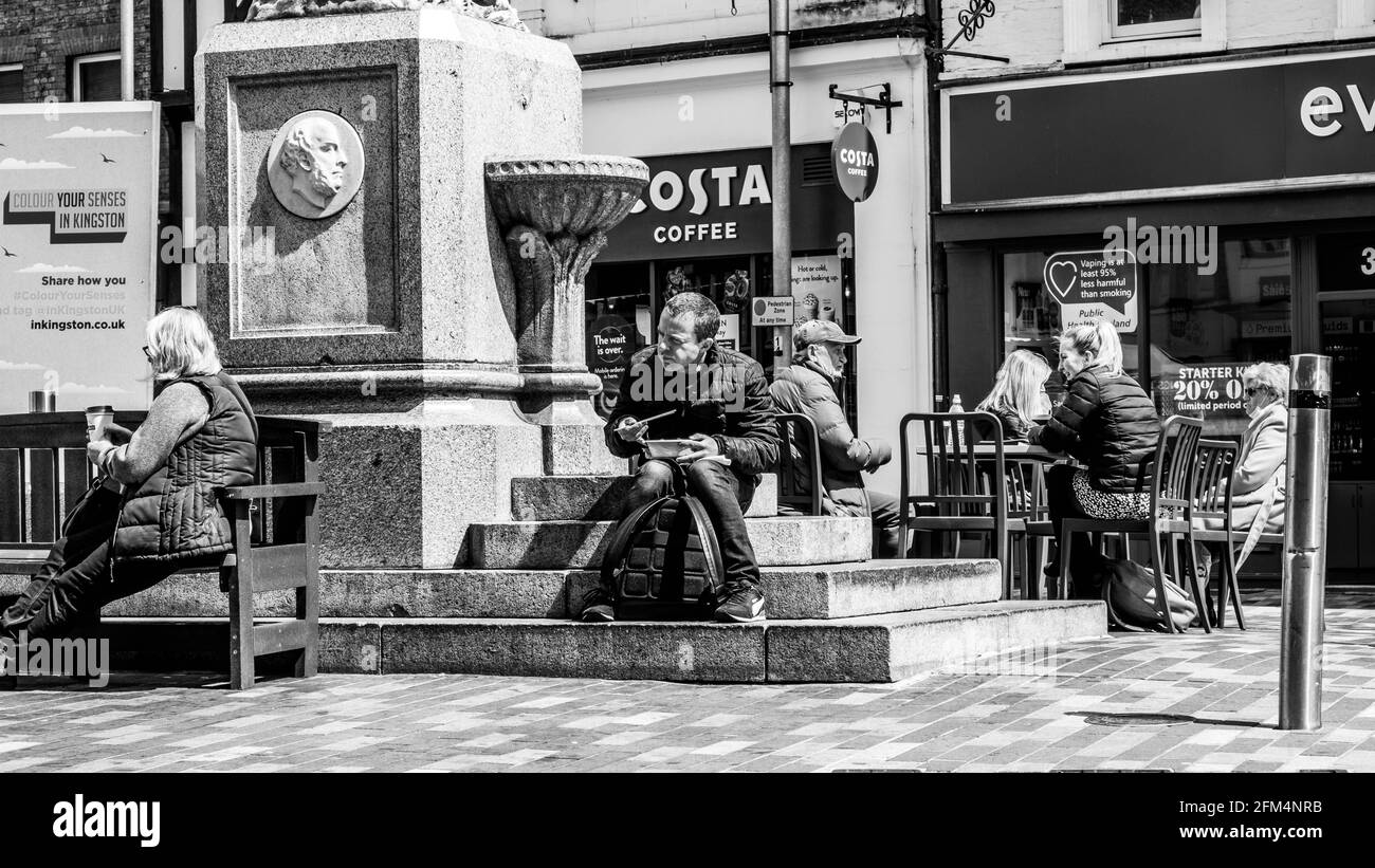 Kingston upon Thames London, Großbritannien, 04 2021. Mai, Black and White Image Mann sitzt auf der Treppe Essen Takeaway Food außerhalb Costa Coffee Shop Stockfoto