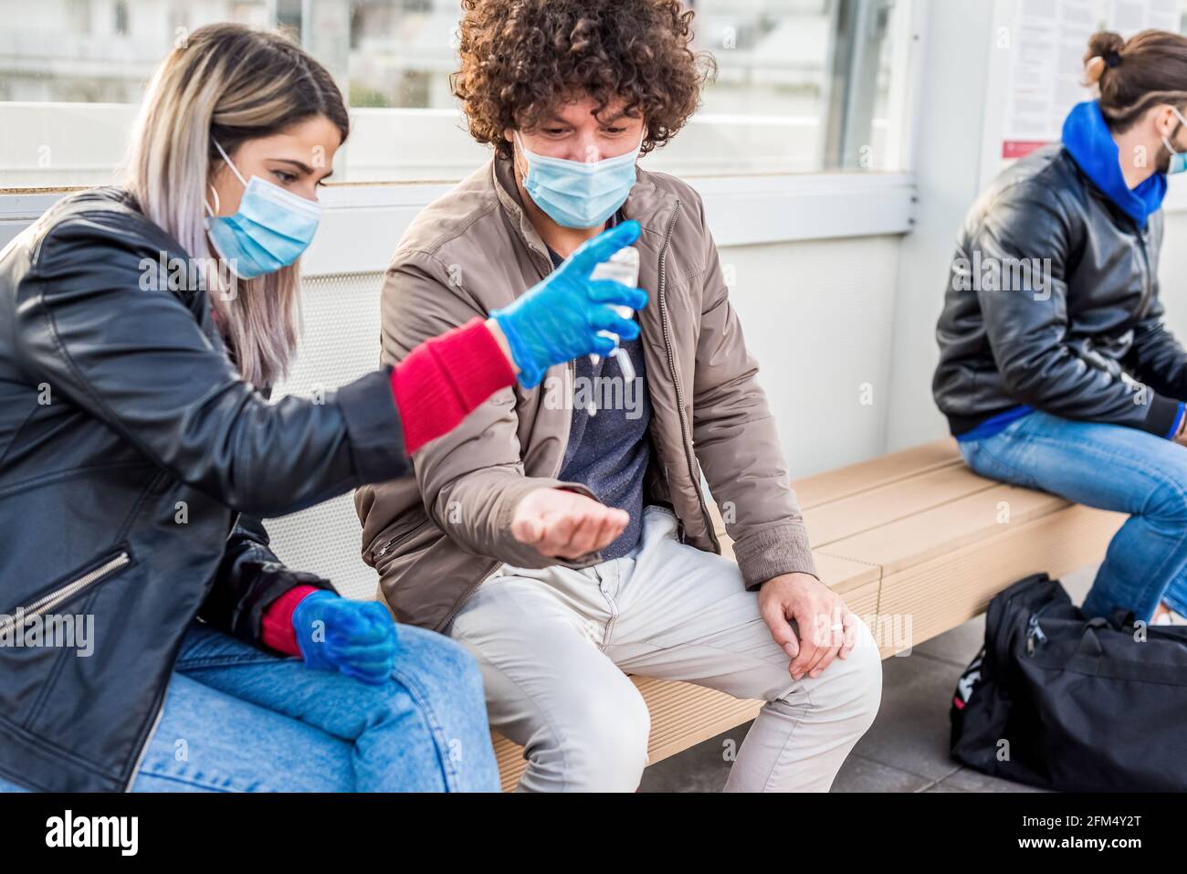 Junges Paar wartet in der Straßenbahnhaltestelle mit Desinfektionsmittel Handgel Tragen einer schützenden Gesichtsmaske, Handschuhe während des Coronavirus-Lockdown-Wiedereröffnungsens.Virus-Ausbruch Stockfoto