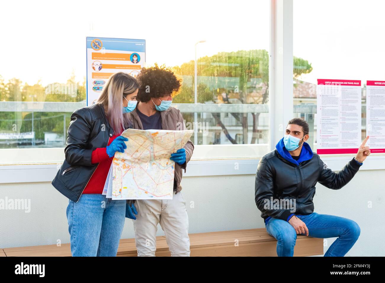 Das junge Paar wartet in der Straßenbahnhaltestelle mit der Touristenkarte Schutzmaske und Handschuhe während des Coronavirus-Lockdown-Wiedereröffnens.Virenausbruch Stockfoto