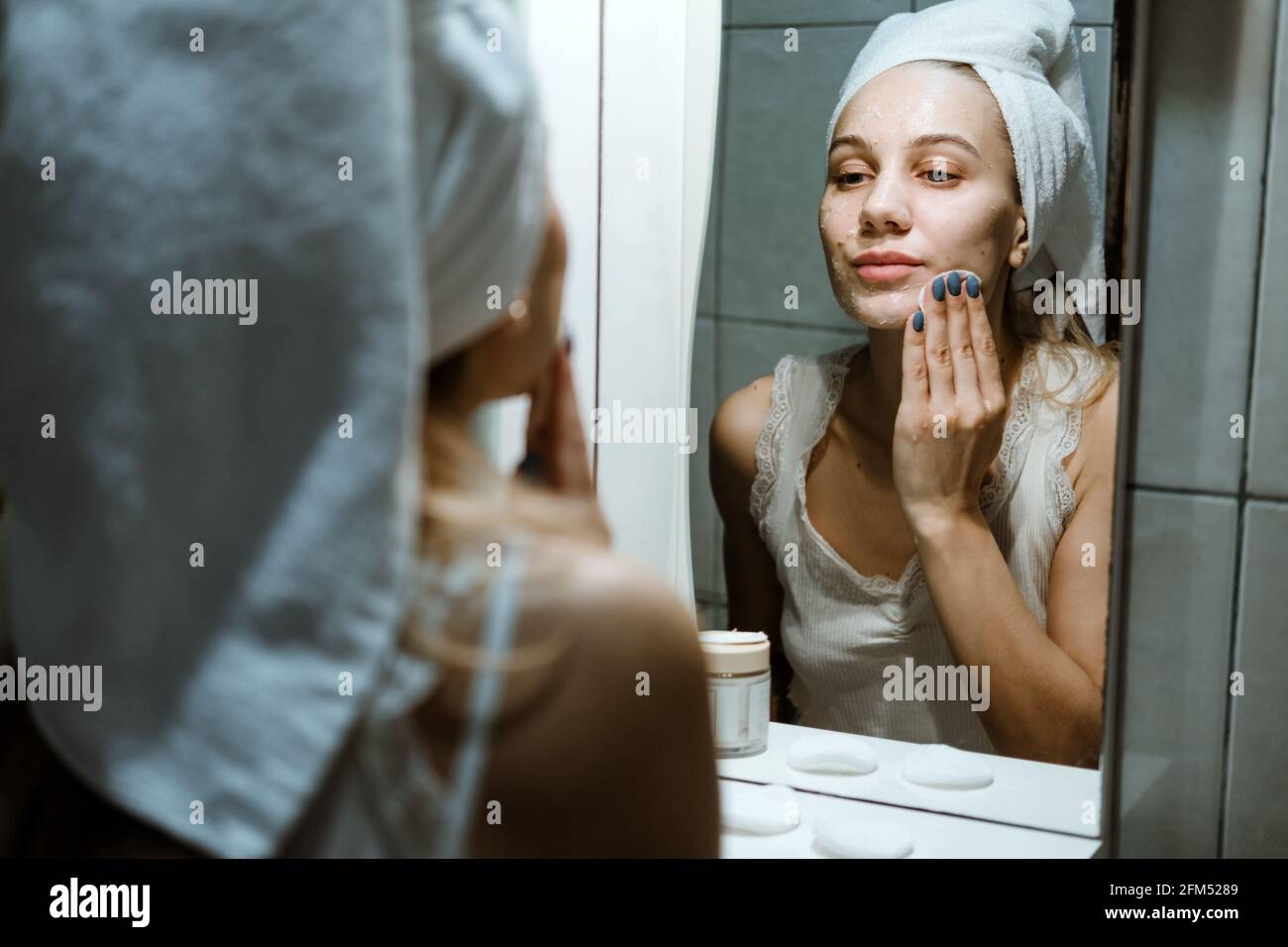 Verwenden Sie Die Gesichtsmaske Zum Abwaschen, Und Verwenden Sie Die Maske Zum Abwaschen Korrekt. Junge Frau im Handtuch auf ihrem Kopf Gesicht waschen, nachdem sie die Maske im Badezimmer entfernt. Stockfoto