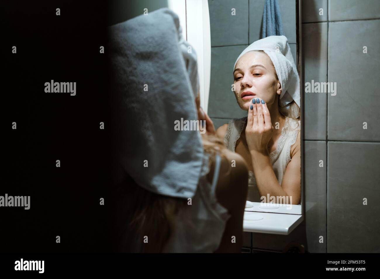 Verwenden Sie Die Gesichtsmaske Zum Abwaschen, Und Verwenden Sie Die Maske Zum Abwaschen Korrekt. Junge Frau im Handtuch auf ihrem Kopf Gesicht waschen, nachdem sie die Maske im Badezimmer entfernt. Stockfoto