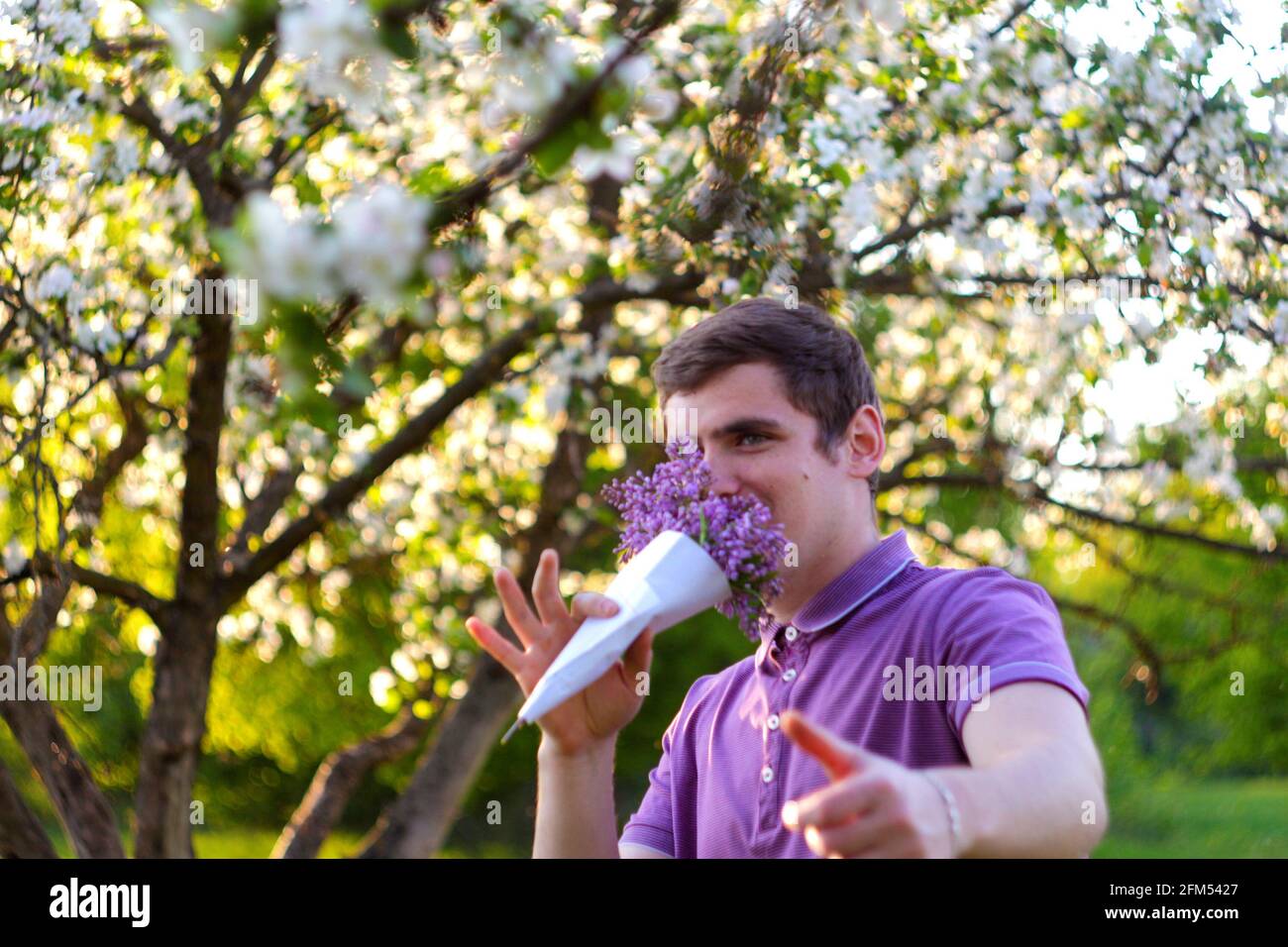 Unschärfe-Porträt eines hübschen kaukasischen Mannes mit Kegelblumen in Flieder Garten Lustige fröhlich junge Brünette Kerl riecht frische Blumen Und betrachten Stockfoto