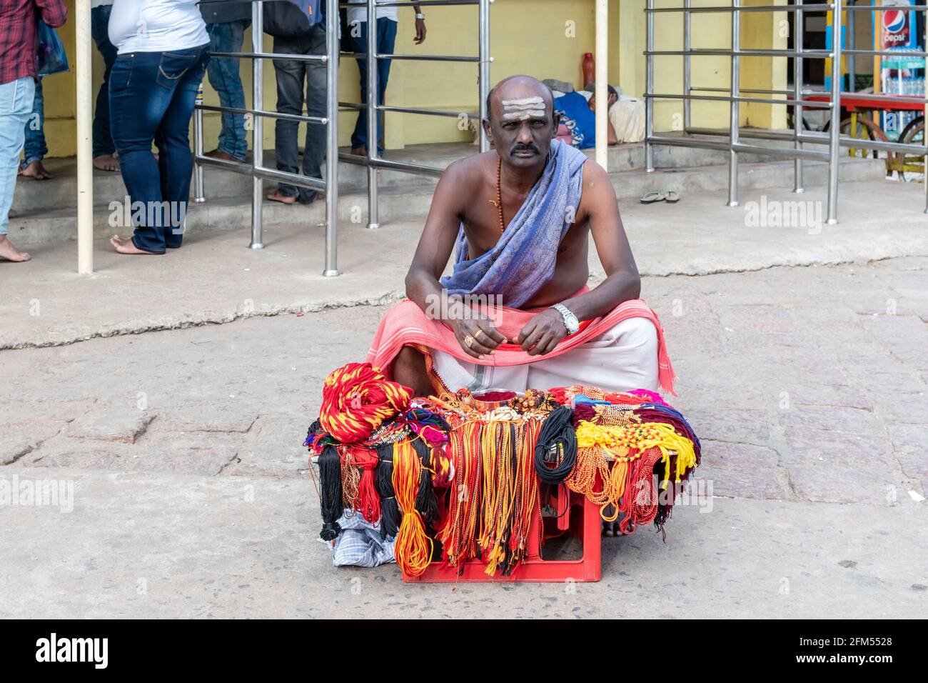 Mysuru, Karnataka, Indien - Januar 2019: Ein indischer Pilger in traditioneller Kleidung, der farbenfrohe Bänder für hinduistische Rituale im alten Tempel in C verkauft Stockfoto