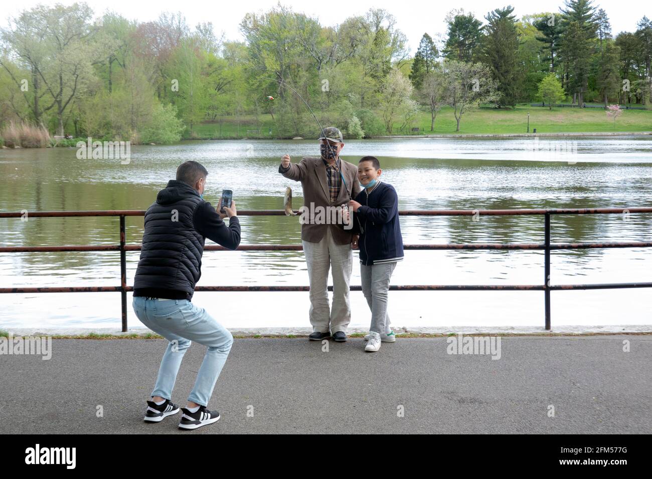 Ein stolzer Junge posiert mit seiner Familie, die den Fisch zeigt, den er gefangen hat. Am See im Kissena Park, Flushing, Queens, New York City. Stockfoto