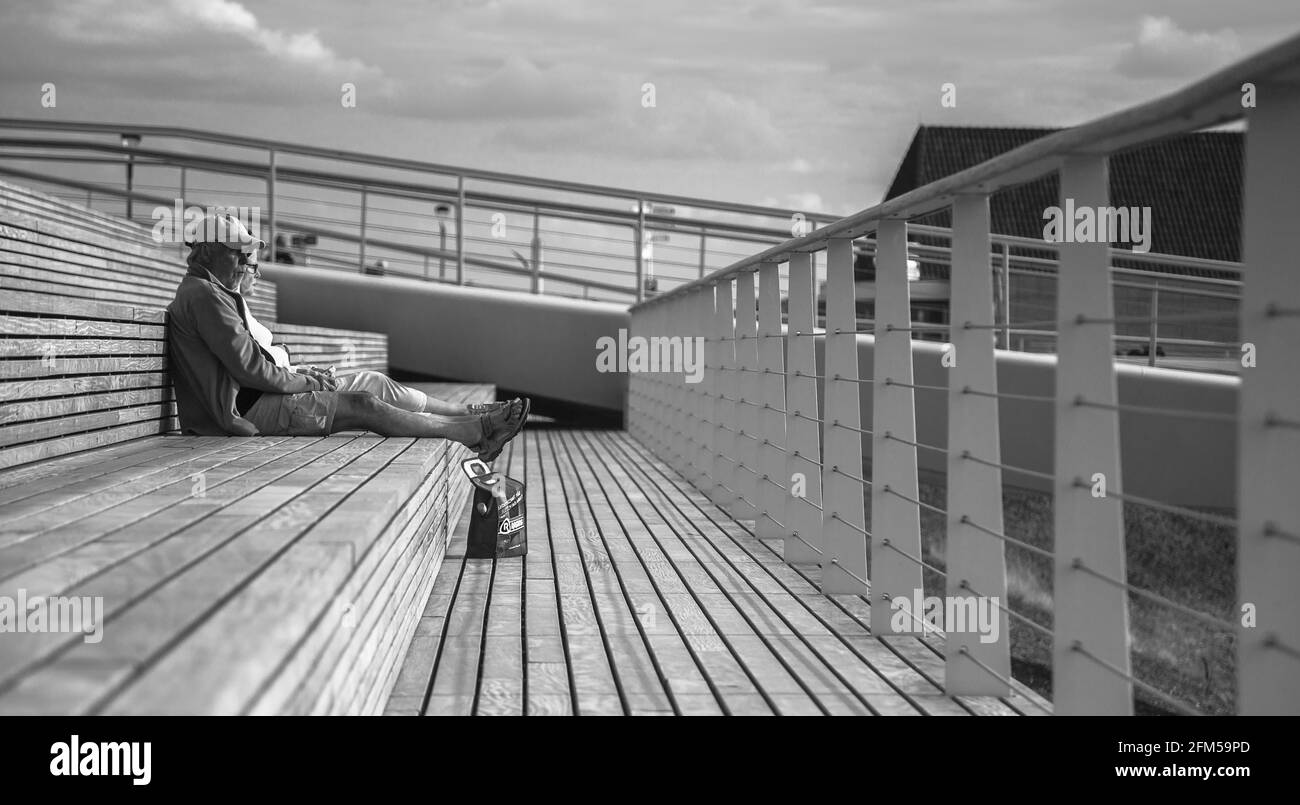 Ein älteres Paar, das sich auf einer Terrasse am Yachthafen entspannen und auf die man blicken kann Im Sommer auf der anderen Seite des Meeres trinken Stockfoto