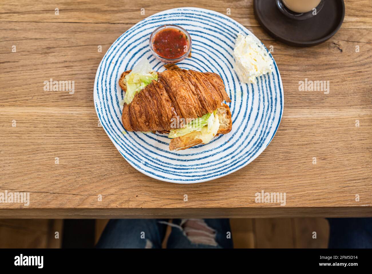 Croissant mit gegrilltem Käse und Salat auf dem Teller, Holztisch im Café, Café. Leckeres Sandwich. Frühstück oder Mittagessen. Stockfoto