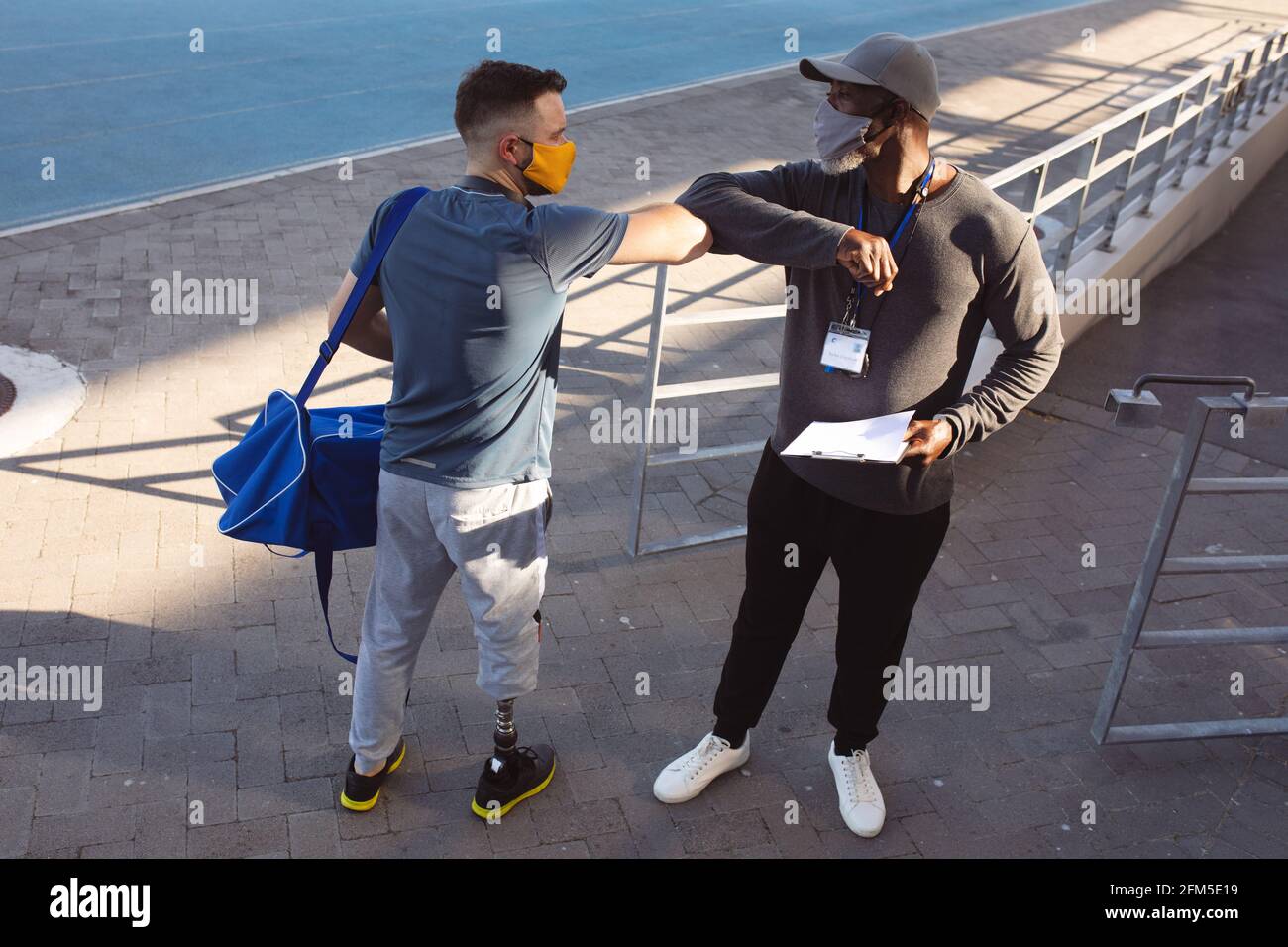 Kaukasischer Athlet mit Beinprothese und afroamerikanischem Trainer Berühren der Ellbogen im Stadion Stockfoto
