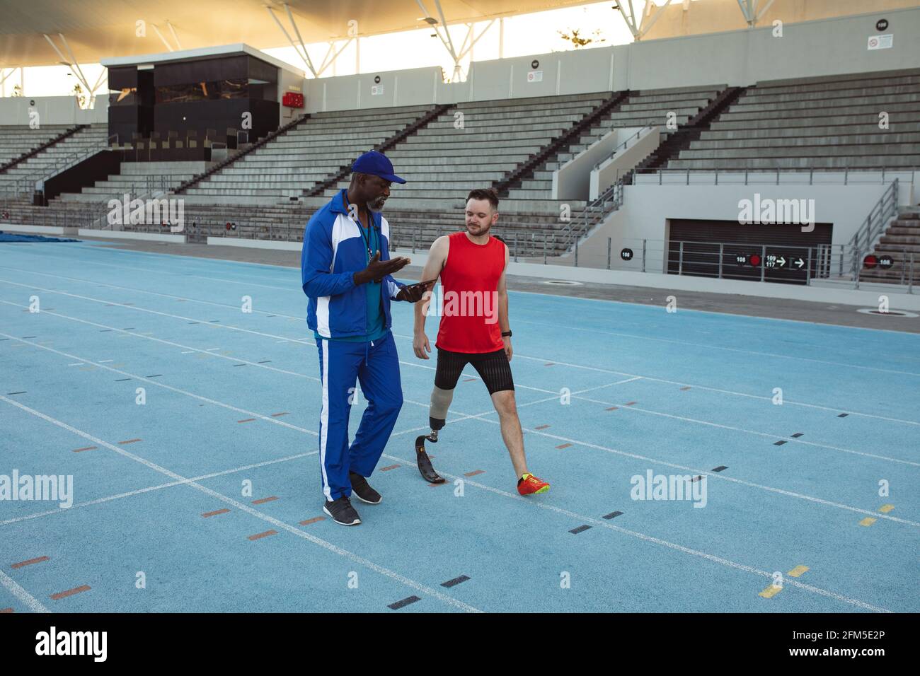 afroamerikanischer Trainer instruiert kaukasischen männlichen Athleten mit Prothesen Bein auf Laufstrecke Stockfoto