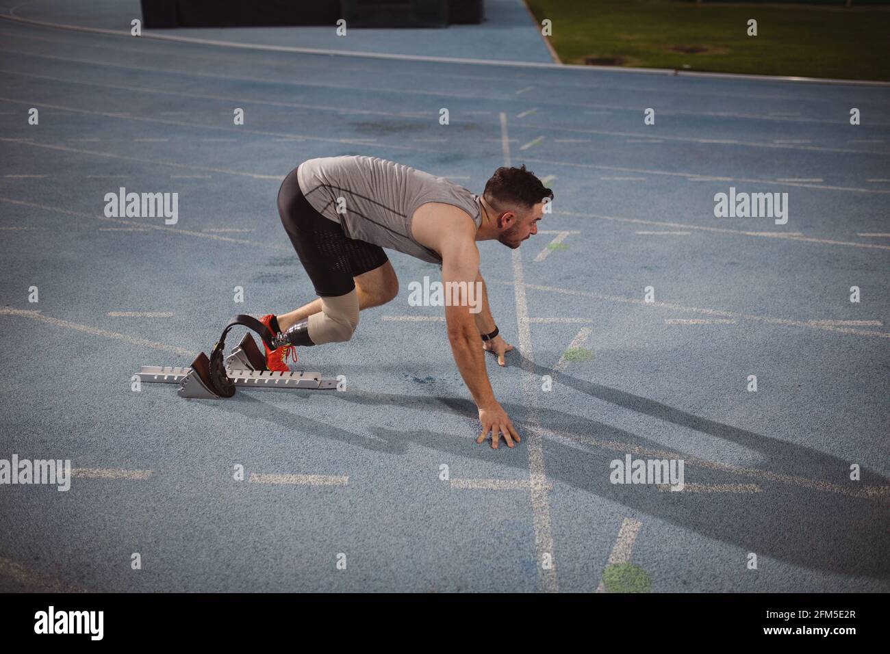 Kaukasischer Athlet mit Beinprothese in Startposition für Nachts auf der Strecke laufen Stockfoto