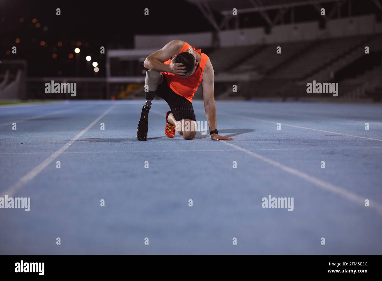Enttäuschter kaukasischer Athlet mit Beinprothese und Hand an Kopf sitzt auf Laufstrecke Stockfoto