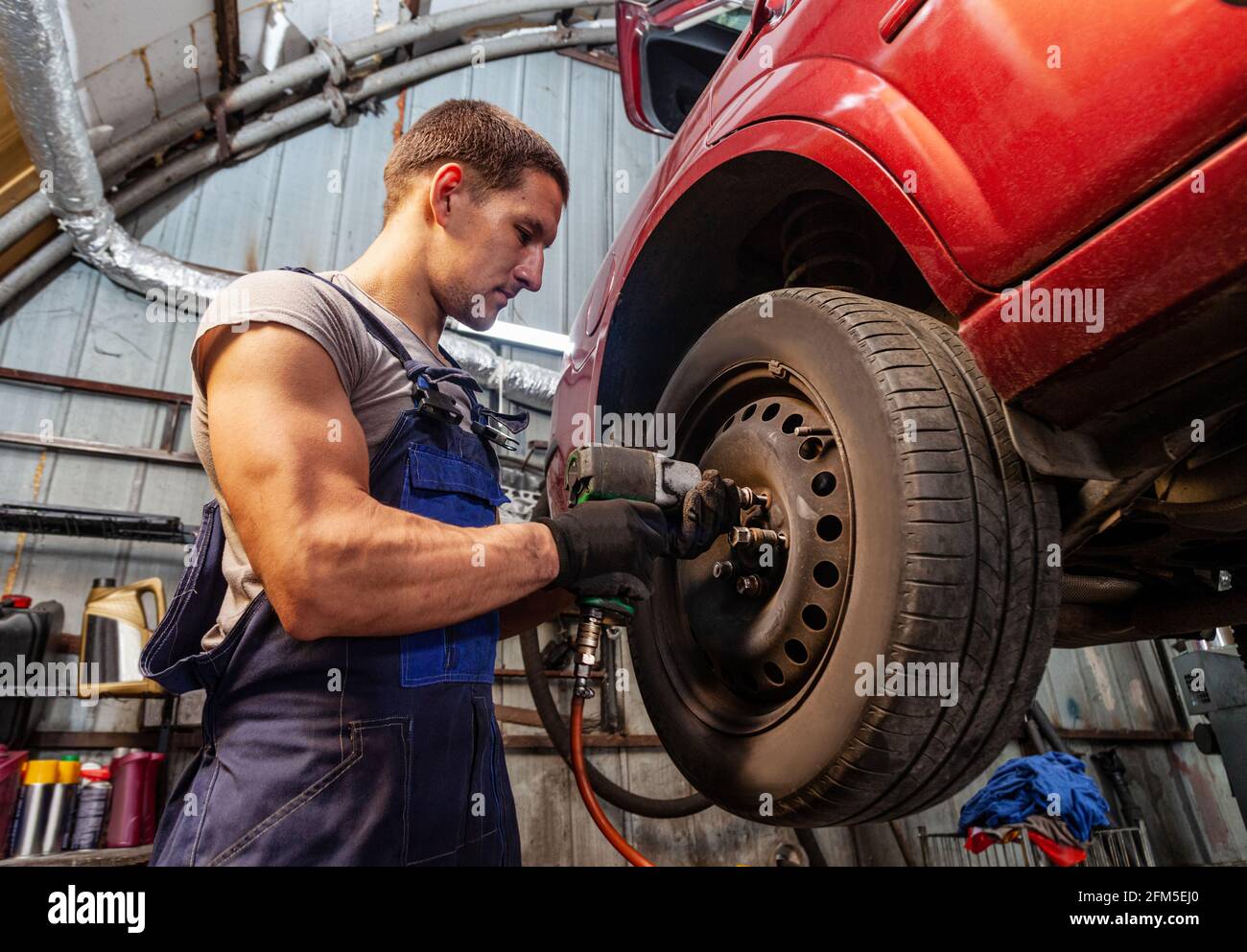 Ein muskulöser Mechaniker hält Räder an einem Fahrzeug in der Autowerkstatt mit pneumatischem Werkzeug. Stockfoto