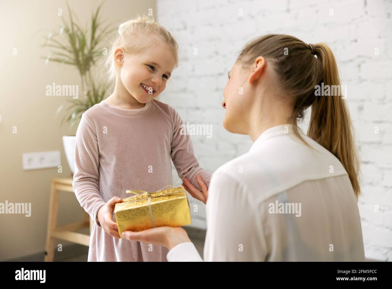 Lächelnde Tochter gibt Geschenk-Box an ihre Mutter zu Hause. Geburtstag oder Muttertag Konzept Stockfoto