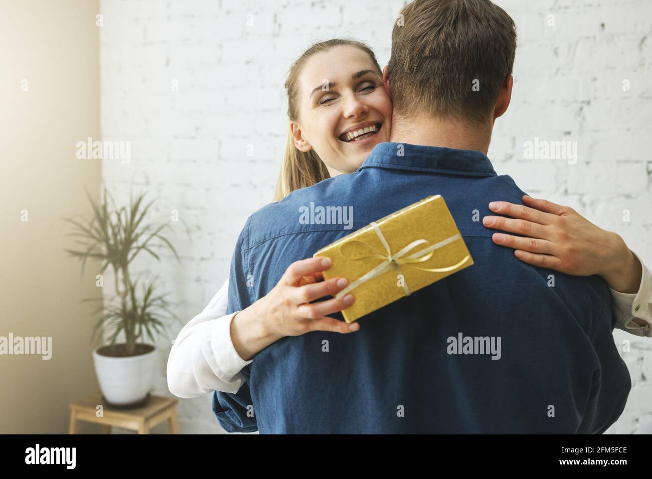 Dankbare Frau mit Geschenkbox umarmenden Ehemann zu Hause. Geburtstag oder Jubiläum Überraschung Stockfoto