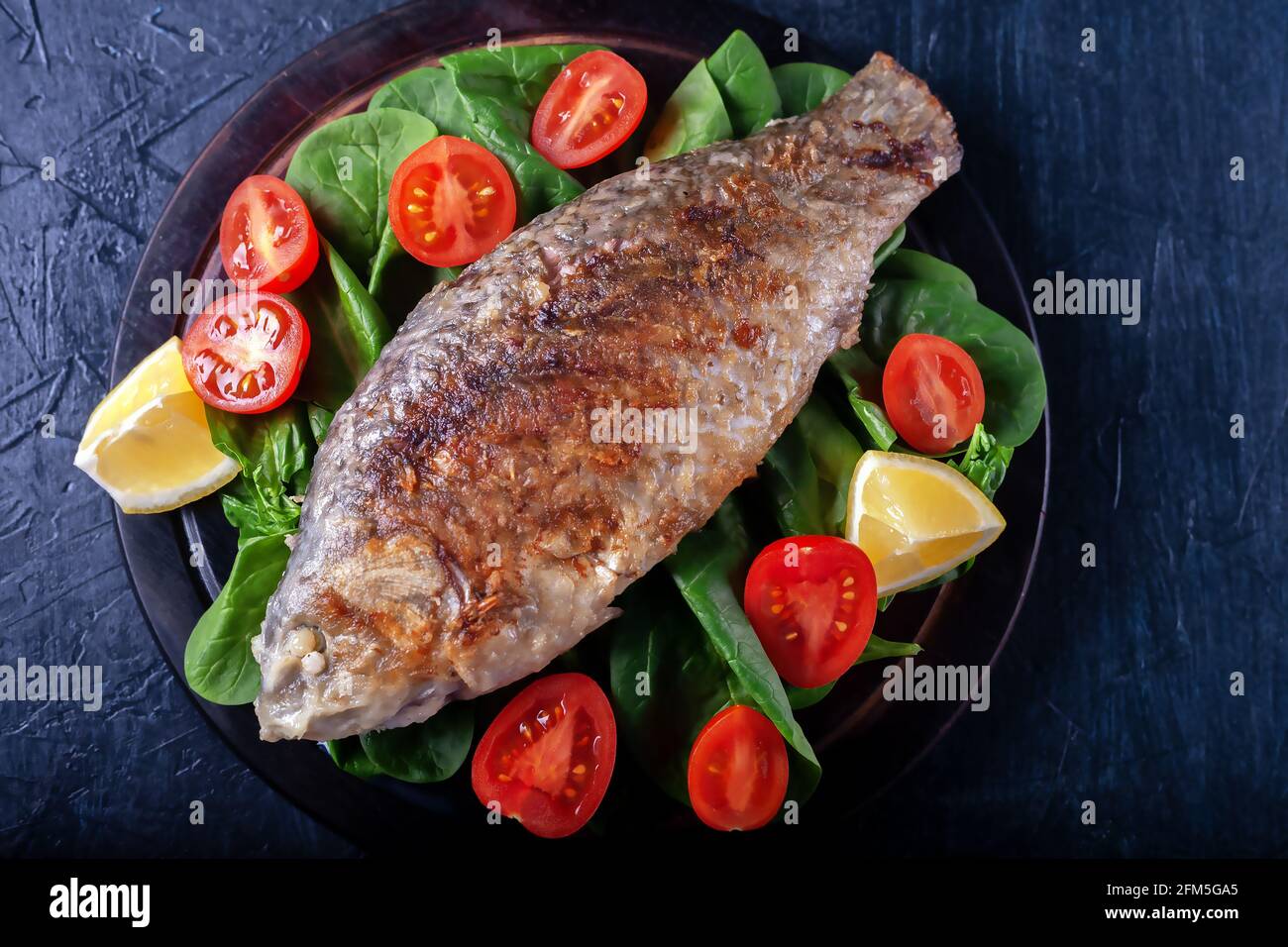 Gegrillter Fisch mit Tomaten, Spinat auf einem Holzbrett. Köstliches und leichtes Abendessen Stockfoto