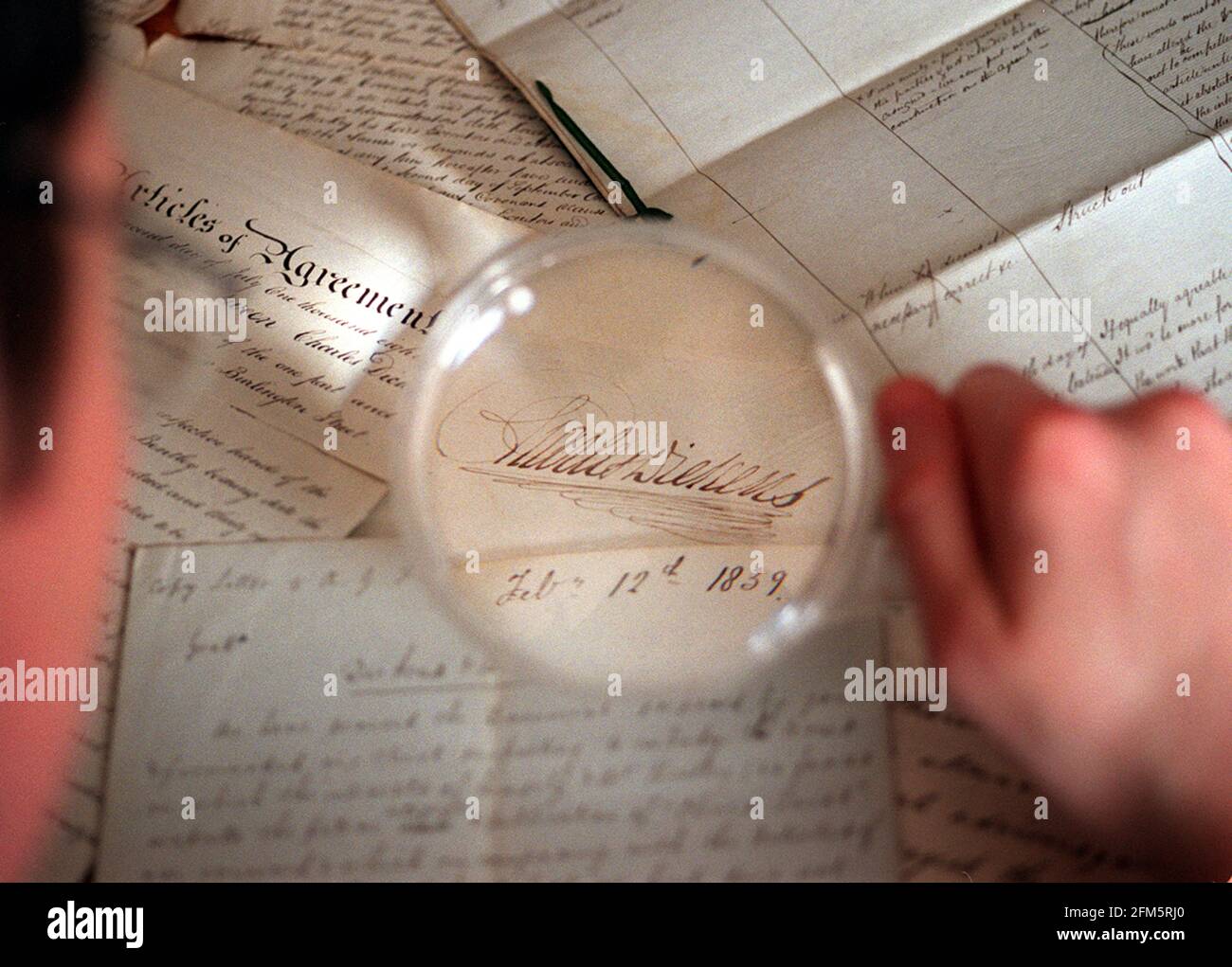 EINE SAMMLUNG VON CHARLES DICKENS-PAPIEREN VOM 2001. FEBRUAR, DIE KÜRZLICH VON DER BRITISCHEN BIBLIOTHEK CRAIG WESTWOOD ERWORBEN WURDE, DER BRITISCHEN BIBLIOTHEK, WIRD BEI DER UNTERSUCHUNG EINIGER DOKUMENTE GESEHEN. UNTER DER LUPE BEFINDET SICH DIE DICKEN'S-UNTERSCHRIFT AUF EINE VEREINBARUNG MIT SEINEM VERLEGER ÜBER DIE VERÖFFENTLICHUNG VON BARNABY RUDGE Stockfoto