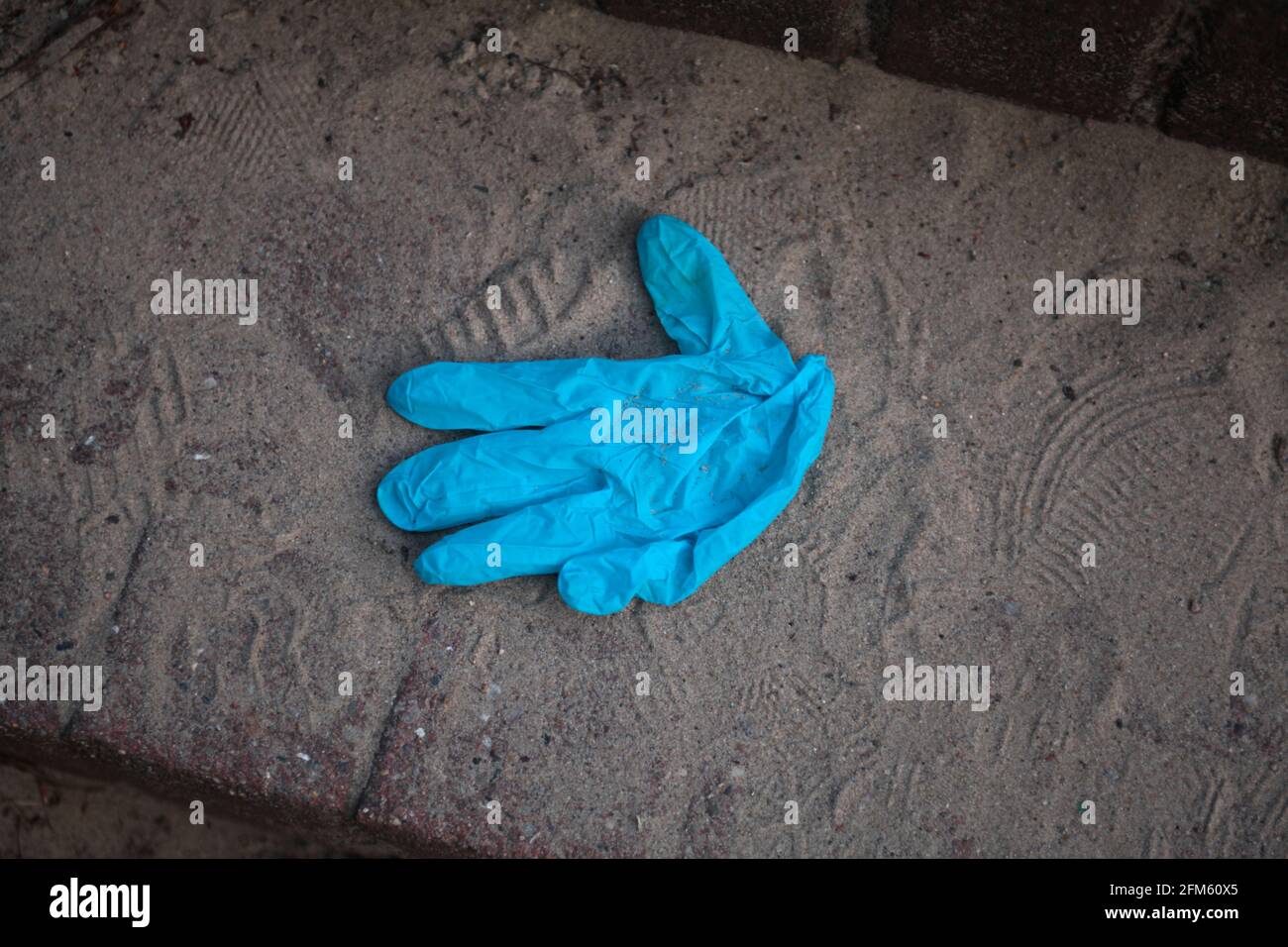 Einweg-Handschuh auf einem sandigen Boden weggeworfen Stockfoto