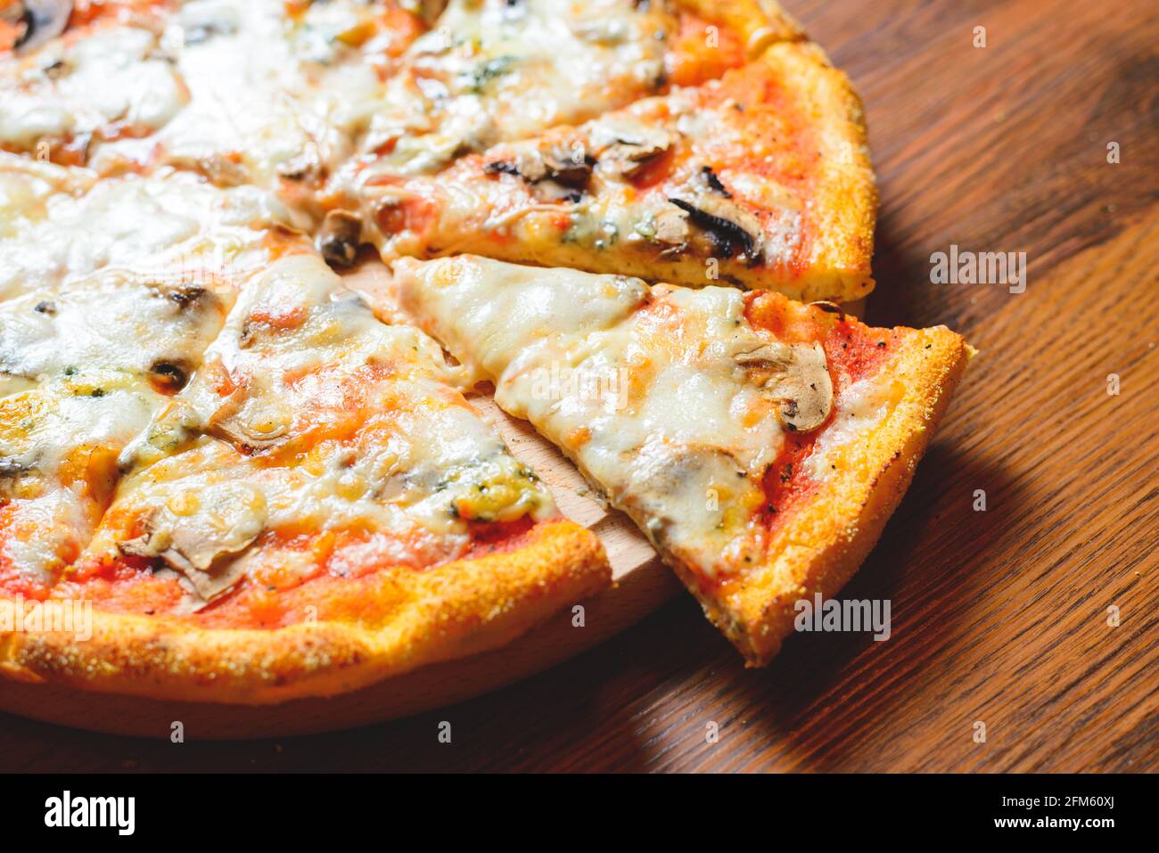 Nahaufnahme der italienischen Pizza, die auf einen Holztisch gestellt wird, während die ausgeschnittene Pizzascheibe aus dem Holzteller ragt. Stockfoto