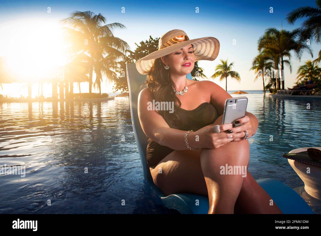 Wunderschöne kurvige Frau, die sich am Pool entspannt und an der Arbeit arbeitet Ihr Telefon Stockfoto