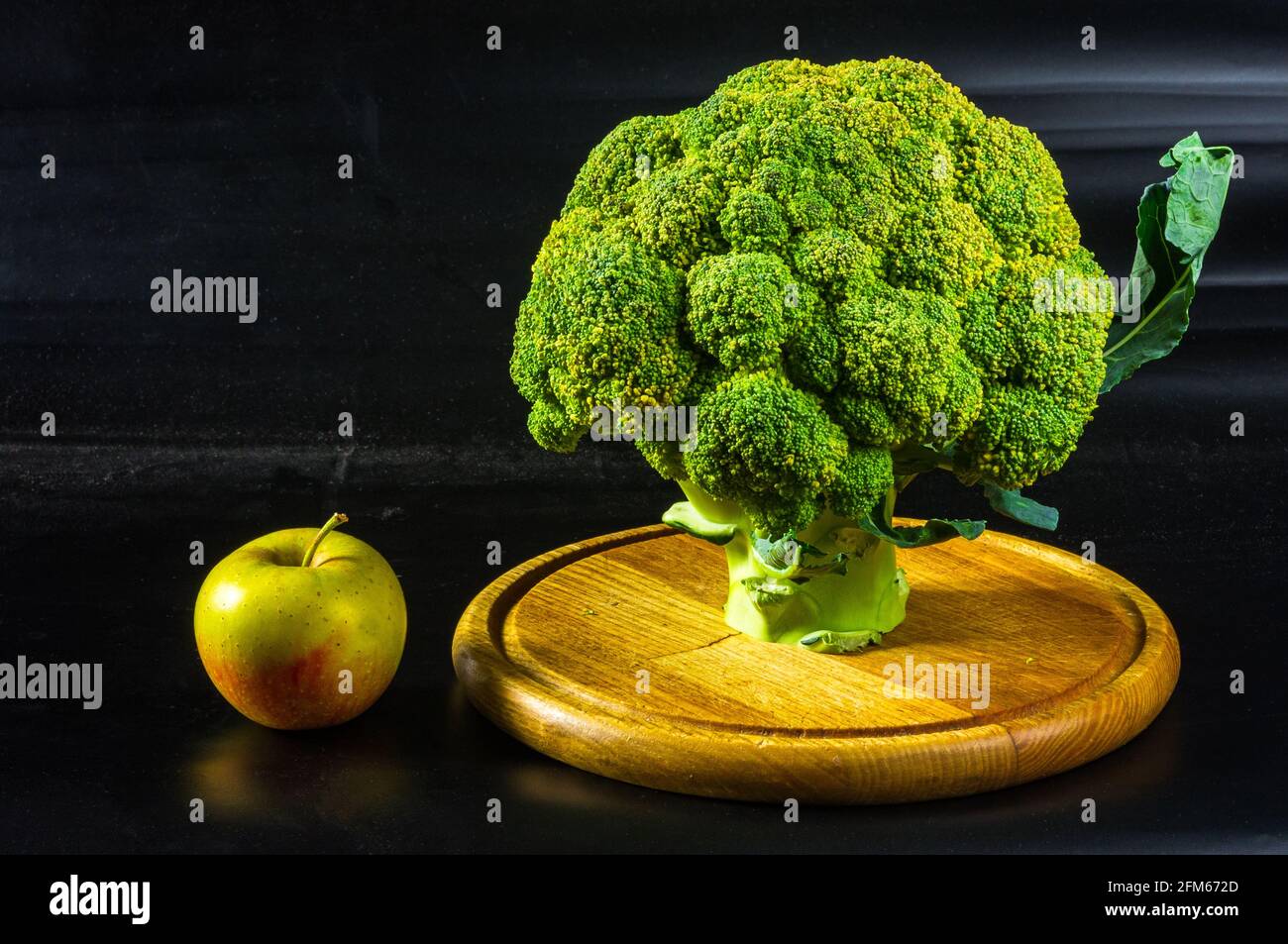 Fantasy Mini Landschaft - Baum mit Brokkoli und Apfel auf schwarzem Hintergrund. Das Konzept des Erscheinens einer Idee, das Symbol von Newtons App Stockfoto
