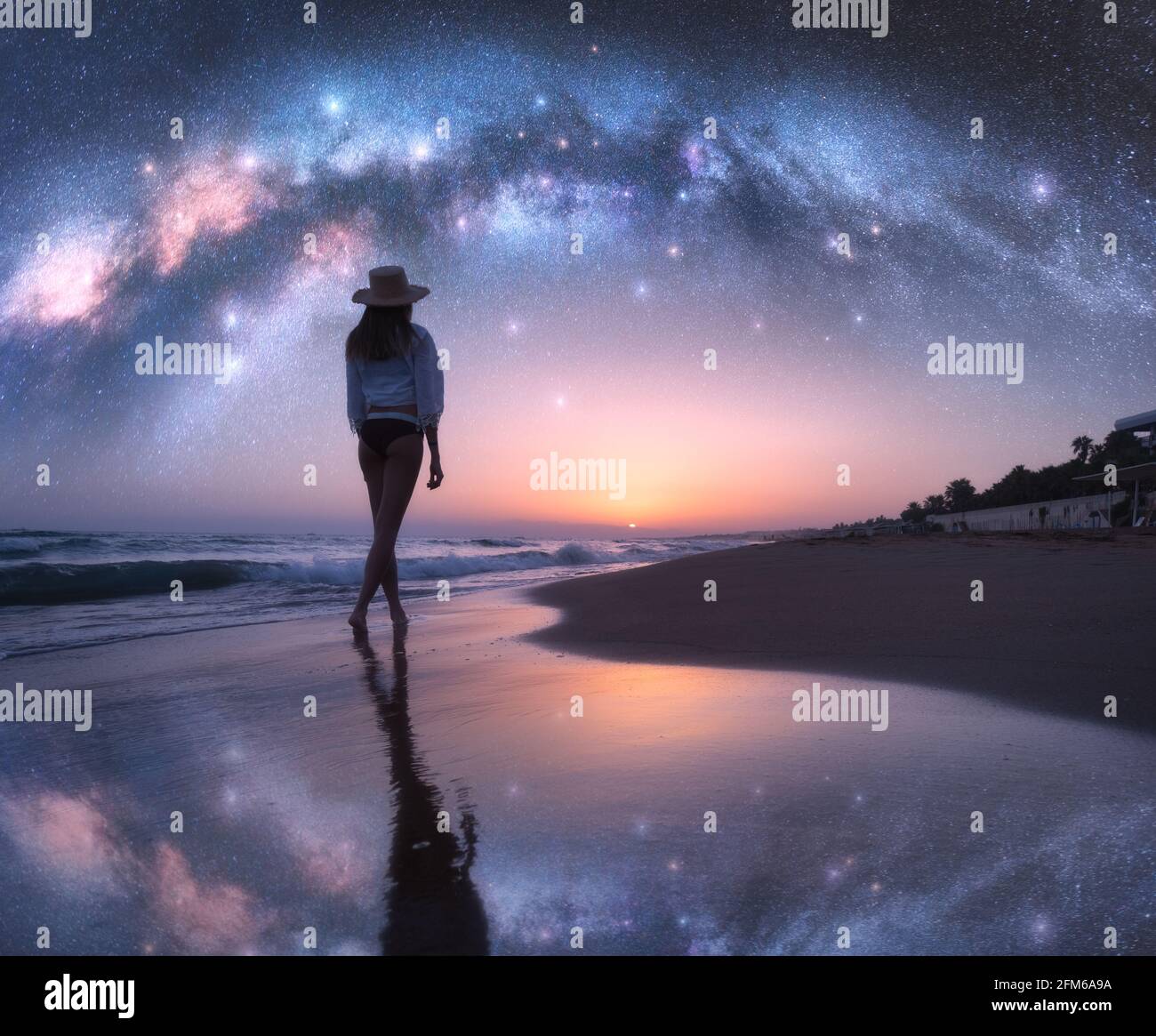 Gewölbte Milchstraße und junge Frau im Hut auf Sand Strand Stockfoto