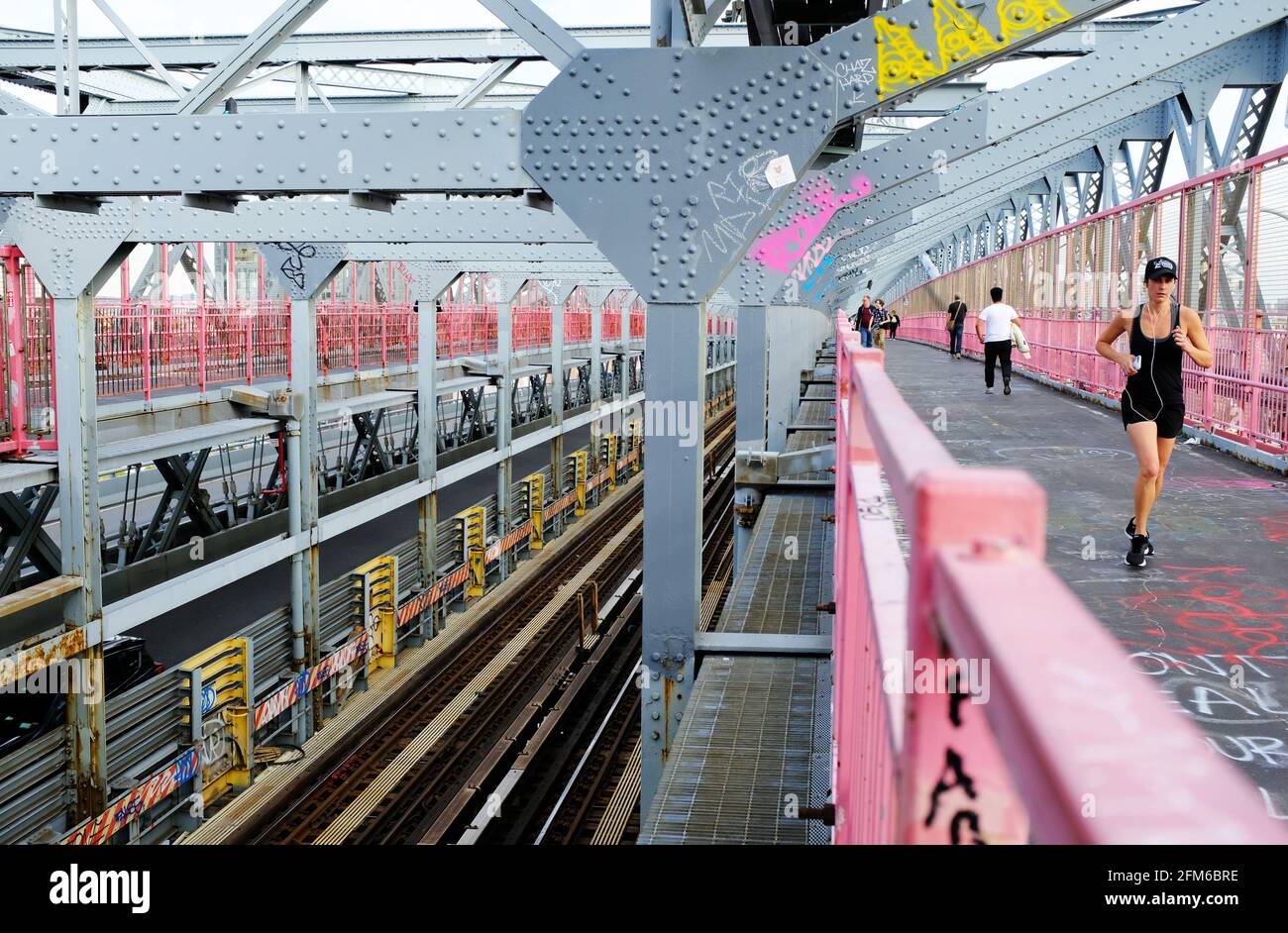 Eine Frau, die auf dem Wanderweg der Williamsburg Bridge joggt Mit U-Bahn-Gleisen daneben.New York City.USA Stockfoto