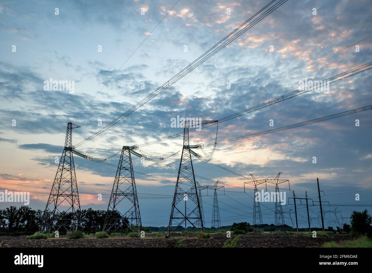 Elektrische Masten und Hochspannungsleitungen im Hintergrund bei Sonnenuntergang. Gruppieren Sie die Silhouette der Sendetürme. Stockfoto