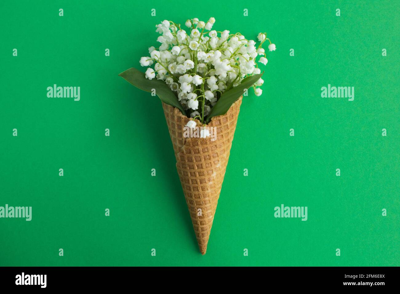 Eis-Kegel mit Lilien des Tals in der Mitte des grünen Hintergrunds.Draufsicht.Copy space.Frühling Blumen Konzept. Stockfoto