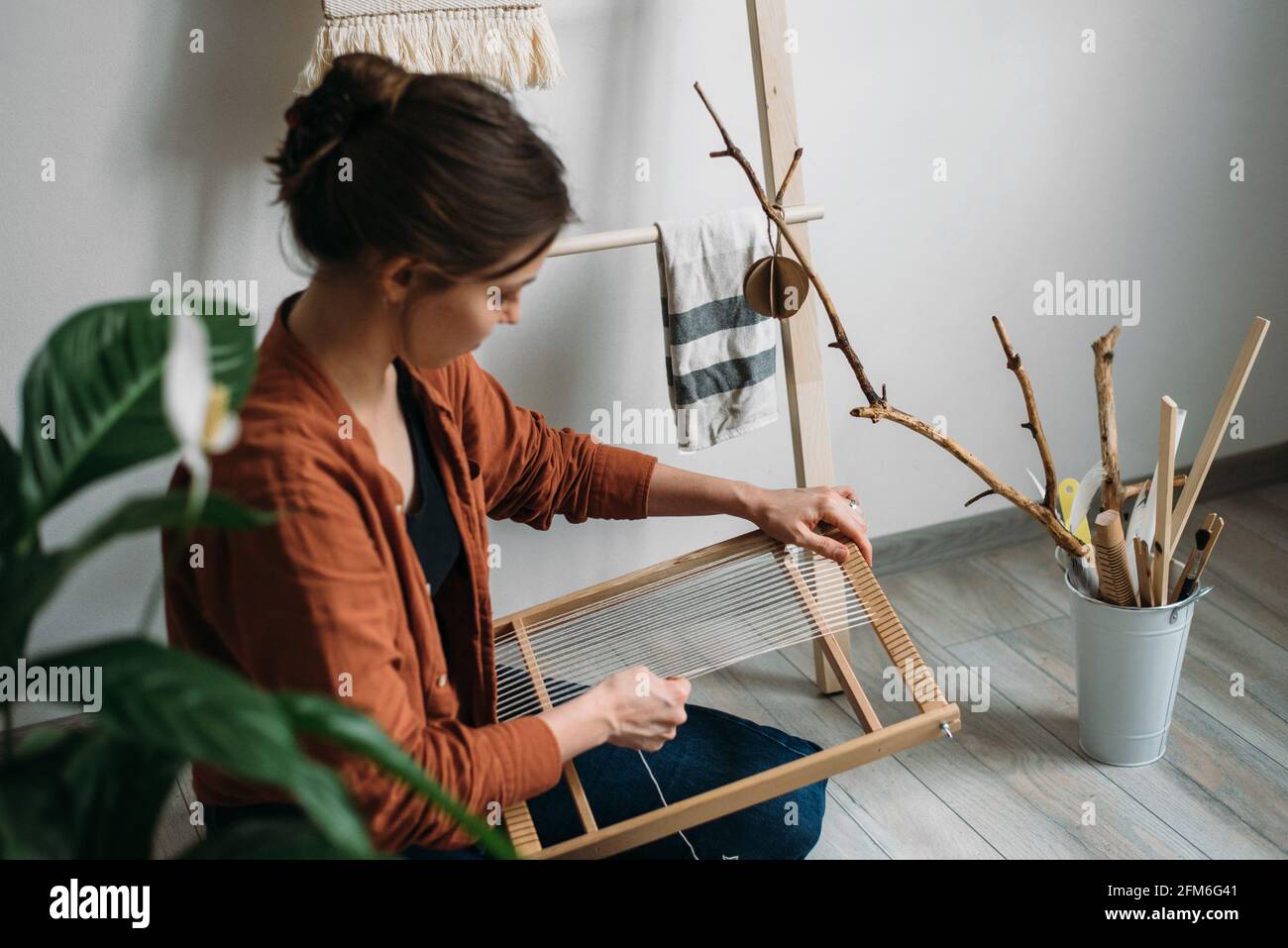 Seitenansicht einer Frau, die einen Wollteppich webt, auf dem sie sitzt Der Boden Stockfoto