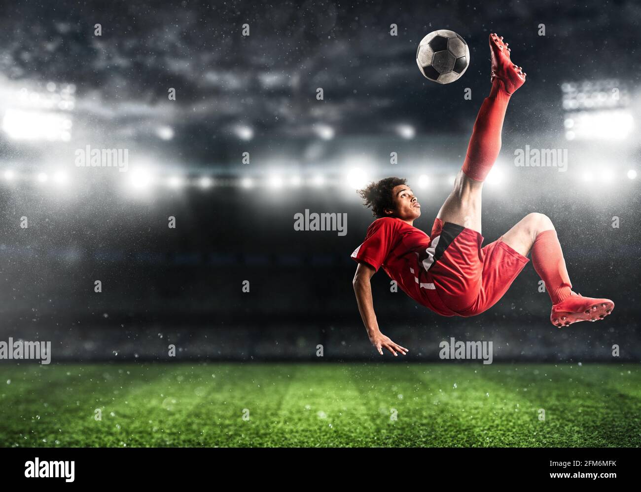 Fußballstürmer in roter Uniform trifft den Ball mit einem Akrobatische Kick in die Luft im Stadion Stockfoto