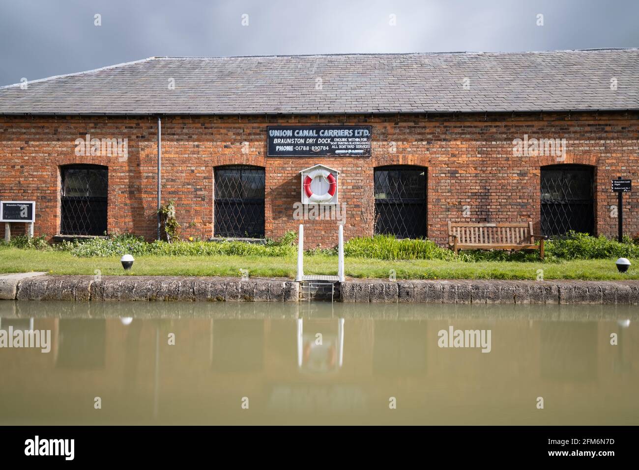 Braunston, Northamptonshire, UK - 5. Mai 2021: United Canal Carriers Werkstattgebäude mit Rettungsschwimmern an Ständern neben einer vollen Kanalschleuse. Stockfoto