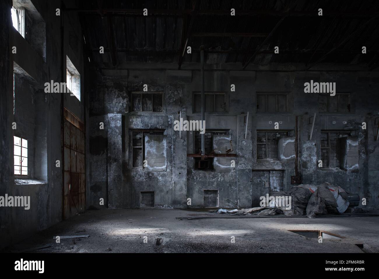 Industriegebäude im Hintergrund. Innenraum einer verlassenen Fabrik mit befleckten Betonwänden, gemauerten Fenstern und alten Geräten Stockfoto