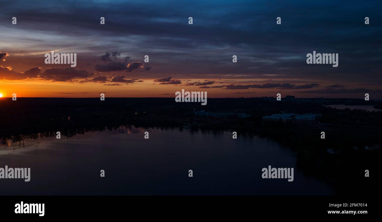 Schöner Sonnenuntergang mit Wolken über dem Fluss unter Bau Häuser in der Dunkelheit, Ukraine, Kiew am 6. Mai. Stockfoto