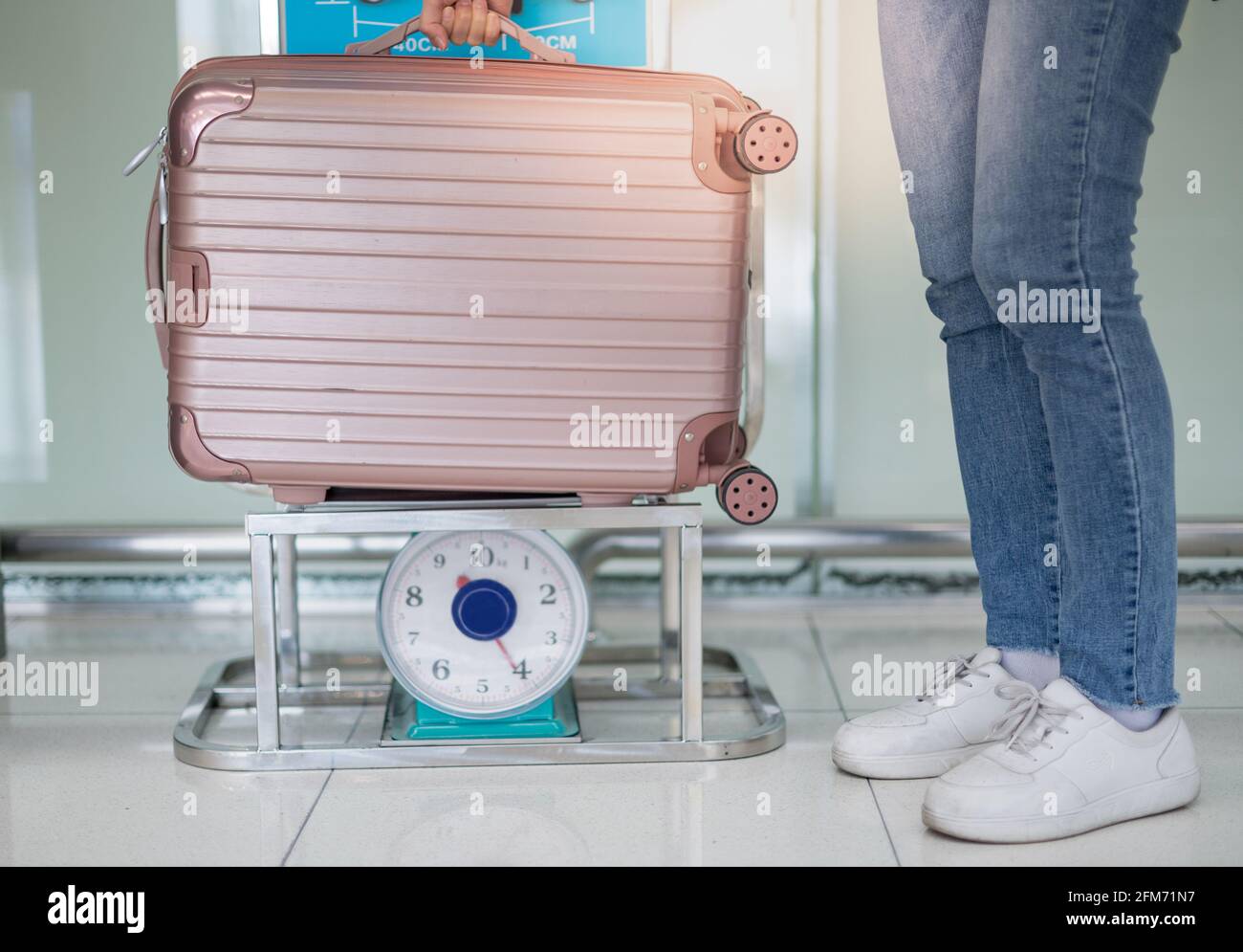 Weibliche Hand, die den Gepäckkoffer auf der Kilo-Waage hält, um das Gewicht zu überprüfen, bereiten Sie den Check-in am Flughafenterminal vor. Stockfoto