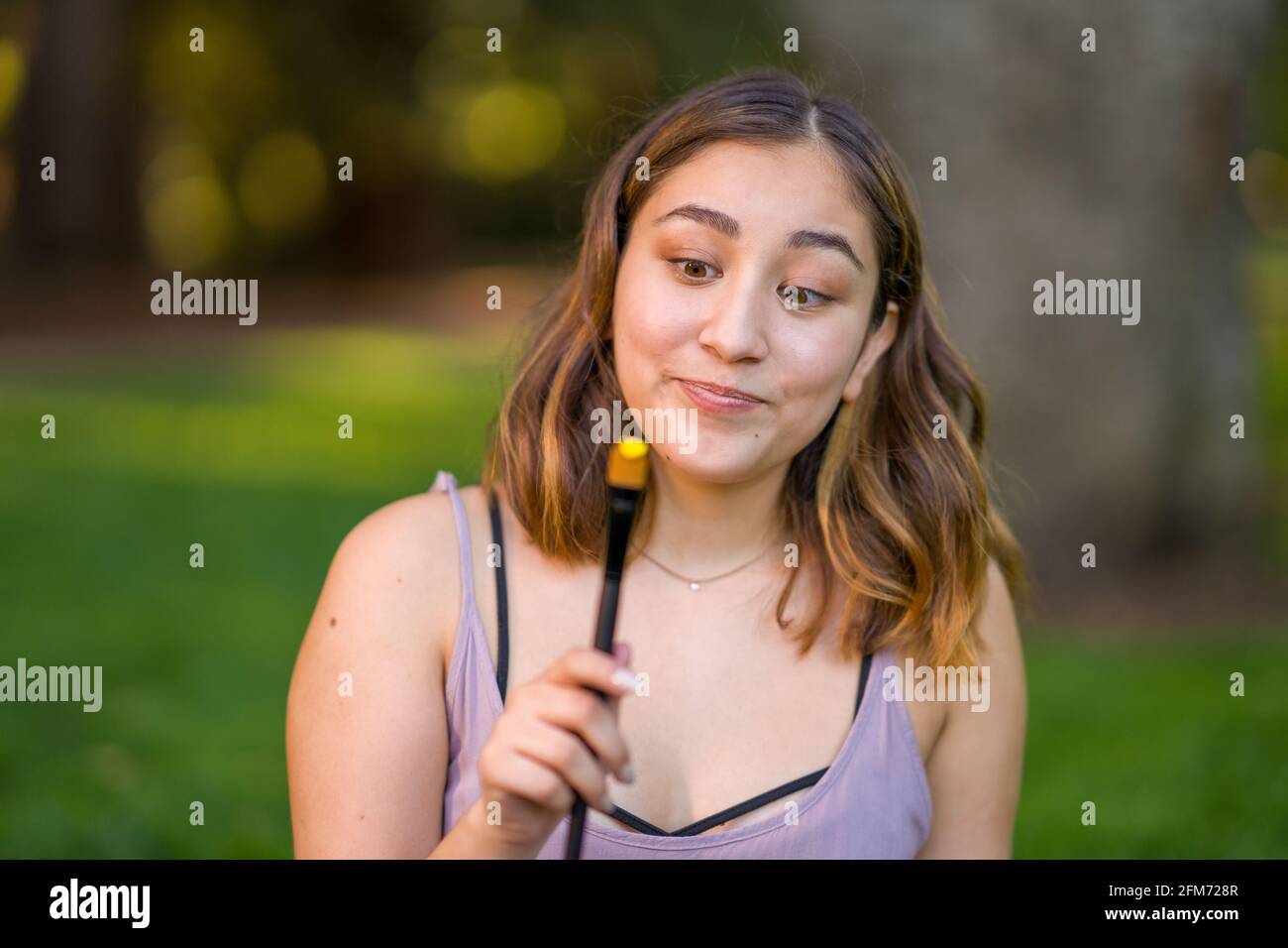 Zierlich jung asiatisch Frau Student Holding ein malen Pinsel mit Gelber Acryllack Stockfoto