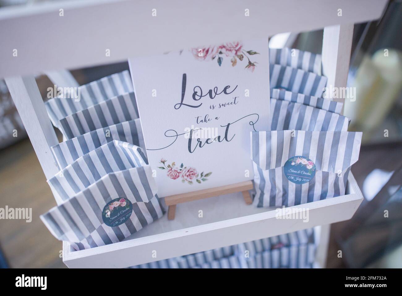 Auf gestreifte graue und weiße Papiertüten mit Süßigkeiten sitzen Ein Regal mit einer Liebe ist ein Leckerbissen-Zeichen Eine Hochzeit Stockfoto