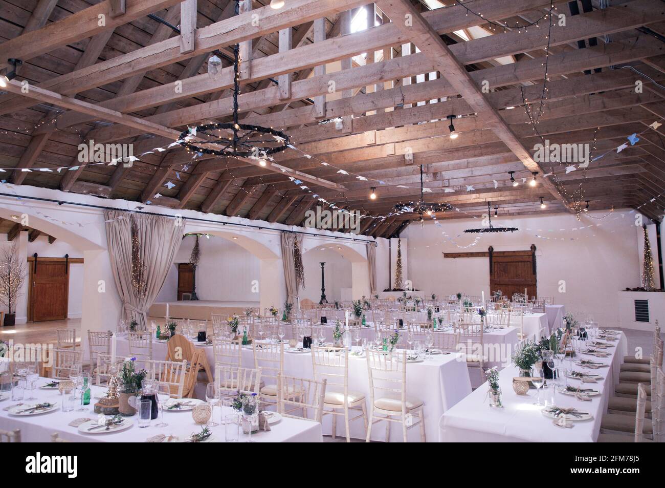 Tische und Stühle für eine rustikale Scheune Hochzeit mit Dachbalken sind zu sehen Stockfoto