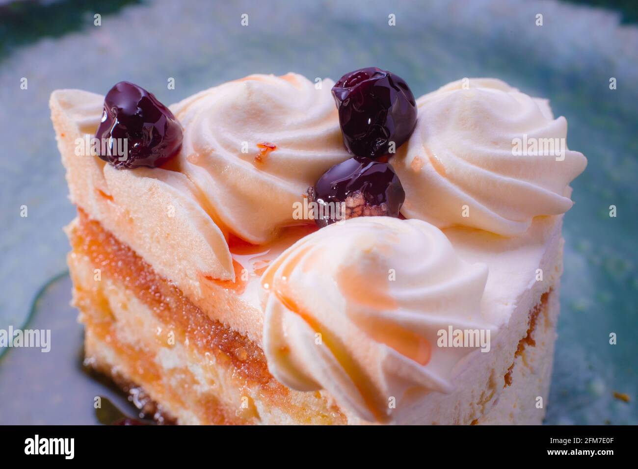 Scheibe Biskuitkuchen mit weißer Creme und Rotkirschsirup. Kuchen auf einem grünen Teller. Stockfoto