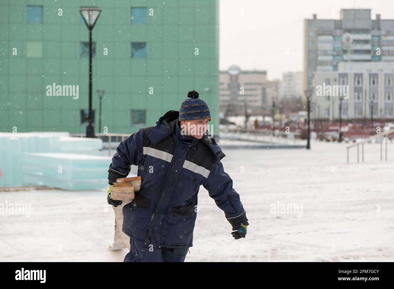 Ein Baumeister in einer blauen Jacke mit Kapuze mit Ein Brett in der Hand geht auf der Baustelle entlang Stockfoto