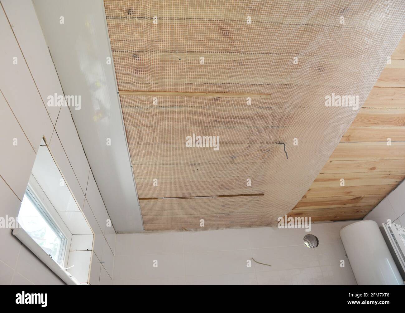 Renovierung des Badezimmers: Installation von PVC-Deckenverkleidungen, Kunststoff-Deckenpaneelen über einer Dampfbarriere-Membran und einer Decke aus bedecktem Holz in einem Badezimmer. Stockfoto
