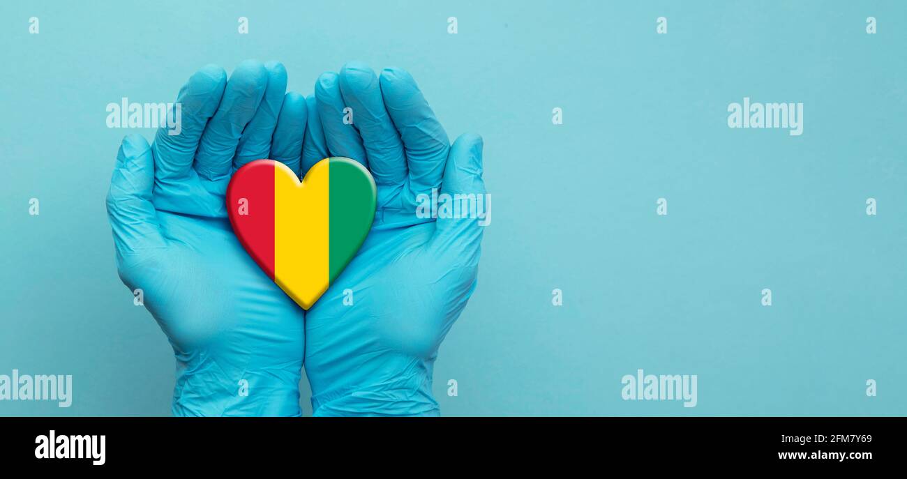 Ärzte tragen chirurgische Handschuhe, die das Herz der Guinea-Flagge halten Stockfoto